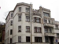 <p style="text-align: justify;">Žymaus tarpukario visuomenės veikėjo ir Kauno miesto burmistro Antano Gravrogko namas pastatytas 1932 metais. Statinys yra vienas iš nedaugelio gyvenamosios paskirties objektų, kuriuos suprojektavo Lietuvos architektūroje išskirtiniu braižu pasižymėjęs E. A. Frykas. Pastatas puikiai atspindi šiam architektui būdingą darnią modernistinių ir istoristinių tendencijų sąveiką. Keturaukščio pastato fasadą sudaro keturi tarpsniai, iš kurių tris apatinius išryškina laužytų formų iškyšos, užsibaigiančios klasikinių formų baliustrados juosiamu balkonu. Balkonas iš abiejų pusių sujungtas su aukštesnėmis šoninėmis fasado dalimis. Kairė fasado dalis ties įvažiavimu į vakarinę sklypo dalį užapvalinta, o dešiniojoje esantis pagrindinis įėjimas, nors ir nėra akcentuotas, tačiau dekoruotas liaudiškų agrarinių bei mitologinių motyvų bareljefais (skulptoriaus Juozo Zikaro 1933 m. sukurti bronziniai bareljefai „Arklių tramdytojas“, „Pjovėjas“, „Rinkėja“). Liaudiško meno akcentais galima laikyti ir antro bei trečio aukšto balkonų puošybą augaliniais motyvais.</p>
<p><em>Pauliaus Tautvydo Laurinaičio</em></p>
<p> </p>