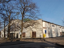<p style="text-align: justify;">Kaunas Sports Hall is one of the most popular and widely covered Lithuanian architectural monuments of the interwar period. The object ordered by the Palace of Physical Culture, together with the football pitch, running tracks, the Palace of Physical Culture (1934), and the national stadium (1935) were part of the sports complex developed near Ąžuolynas. The European Male Basketball Championship held in 1939 even granted this place an international status. Not only because of Lithuania’s triumph, but also thanks to the modern basketball arena. European basketball functionaries at that time considered the hall to be “the only hall in Europe of such quality” designed specifically for basketball.</p>
<p style="text-align: justify;">However, despite its international significance, the construction of the hall was limited not only by time (the hall was finished in half a year), but also by the lack of financial resources: “The goal was to have a building with maximum capacity by using cheapest measures”. Nevertheless, we can argue that the architectural expression of the building was hardly affected by that. On one hand, we had a building of impressive technical characteristics: “The hall, capable of housing eleven thousand spectators (3.5 thousand seated), was 63 m long, 61 m wide and 15.2 m high in the middle. Technical design was based on four bolted steel arches of 61 m, set apart from each other by 13.2 m, and resting on strong 80 m<sup>3</sup> reinforced concrete foundations. Each arch, weighing 12 tons, consisted of 12 sections. The walls were made of metal frachverch construction, the stands were wooden, and the roof was out of boars covered with roofing felt.” On the other hand, utilitarian construction represented <em>existensminimum</em> ideals characteristic of international modernist architecture of that time.</p>
<p style="text-align: justify;">Hence, an ascetic and plain, yet monumental in its scope the building became a real monument to Lithuanian zeitgeist at that time. However, it is interesting to note that people had differing opinions on the architecture of the building at the time of its building. For example, weekly magazine on culture, literature and art Naujoji Romuva<em> </em>published a text in 1939, signed by initials A. T., whose author called the sports hall a “failure” and “ugly” and argued that “it is unlikely that there will be anyone who can say that it is a highlight”.</p>
<p style="text-align: justify;"><em>Vaidas Petrulis</em></p>